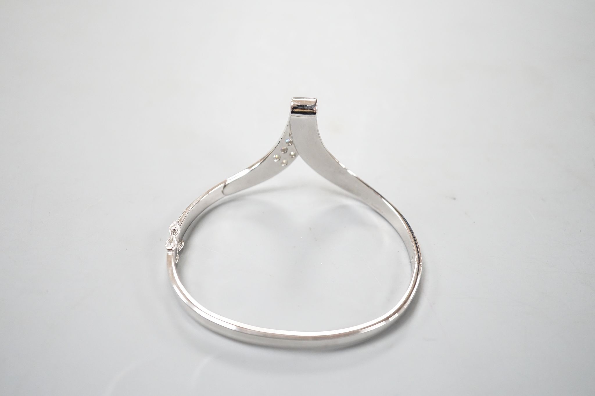 A modern 585 white metal and twelve stone diamond set wishbone shaped hinged bangle, gross 19.7 grams.